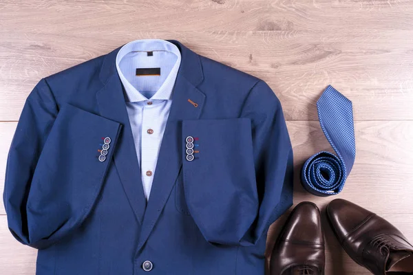 Flat lay conjunto de roupas clássicas dos homens, como terno azul, camisas, sapatos castanhos, cinto e gravata no fundo de madeira . — Fotografia de Stock