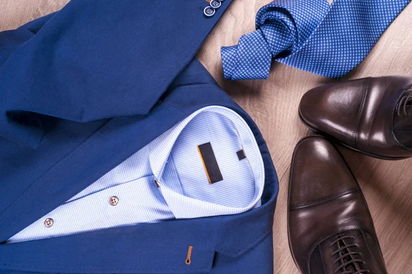 Z płaskim leżał zestaw klasyczne męskie ubrania, takie jak niebieski garnitur, koszule, brązowe buty, pas i krawat na podłoże drewniane. — Zdjęcie stockowe