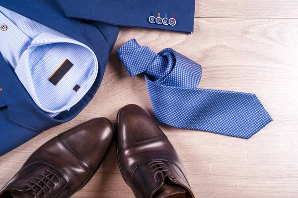 Плоский набор классической мужской одежды, такой как синий костюм, рубашки, коричневые туфли, пояс и галстук на деревянном фоне . — стоковое фото