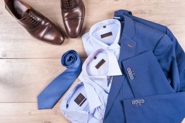 Набор классической мужской одежды - синий костюм, рубашки, коричневые туфли, пояс и галстук на деревянном фоне. — стоковое фото