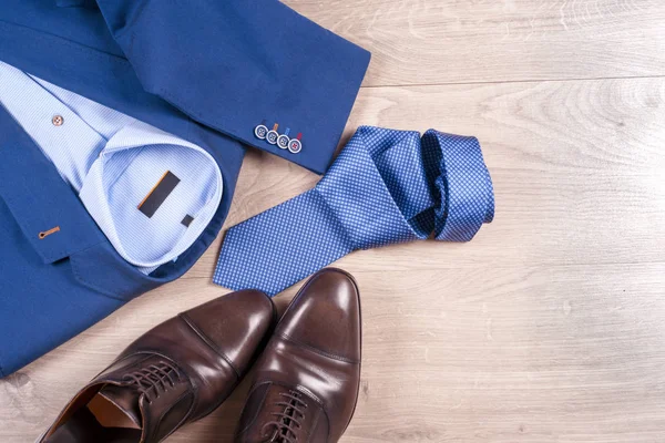 Set klassieke herenkleding - blauw pak, shirts, bruine schoenen, riem en stropdas op houten achtergrond. — Stockfoto