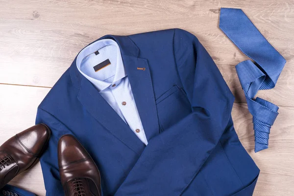 Sada klasických pánských oděvů - modrý oblek, košile, hnědé boty, opasek a kravata na dřevěném pozadí. — Stock fotografie