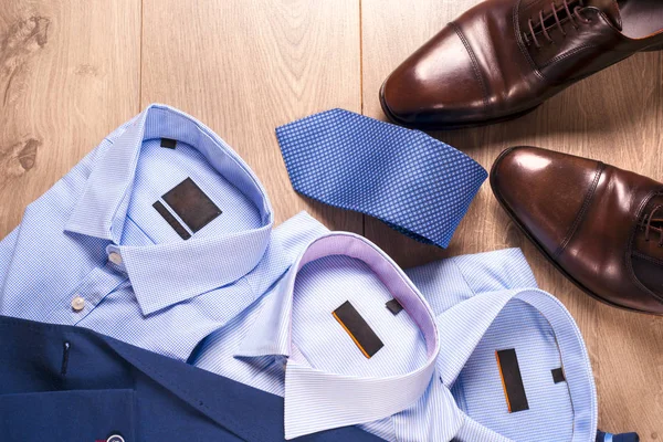 Set klassieke herenkleding - blauw pak, shirts, bruine schoenen, riem en stropdas op houten achtergrond. — Stockfoto