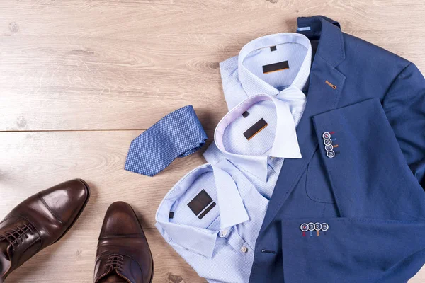 Zestaw klasycznych męskich ubrań - niebieski garnitur, koszule, brązowe buty, pasek i krawat na drewnianym tle. — Zdjęcie stockowe