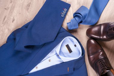 Klasik erkek kıyafetleri - mavi takım, gömlekler, kahverengi ayakkabılar, kemer ve kravat ahşap arka planda.