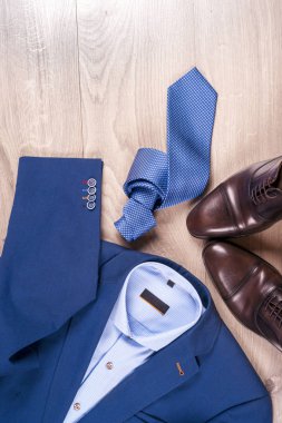 Klasik erkek kıyafetleri - mavi takım, gömlekler, kahverengi ayakkabılar, kemer ve kravat ahşap arka planda.
