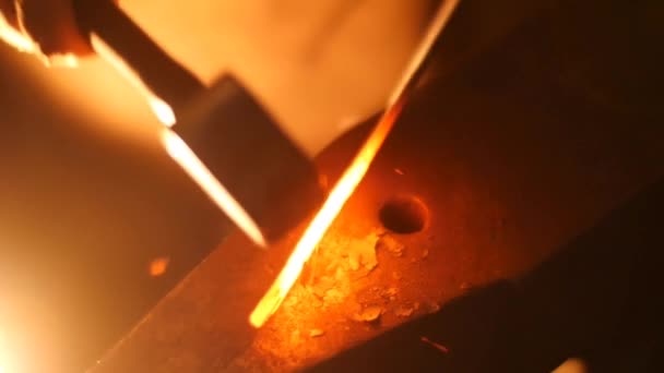 Un forgeron ramasse un marteau massif et commence à frapper une barre métallique chaude sur l'enclume 