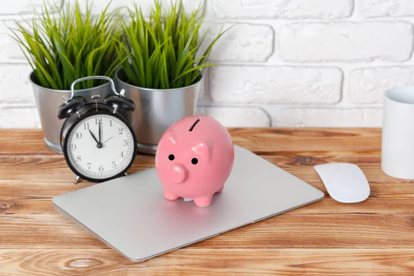 Piggy money box with laptop on wooden table