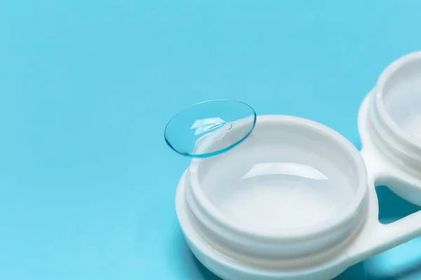Contact lens, contact lens case, tweezers on blue background