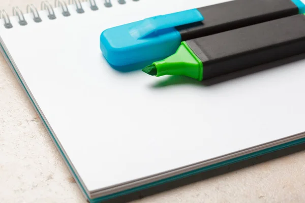 Los iluminadores azules y verdes en la hoja de papel del bloc de notas en blanco yacen sobre un escritorio — Foto de Stock