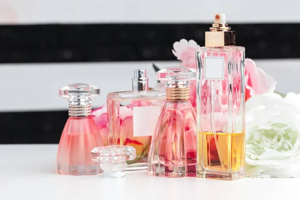 Flessen van parfum met bloemen op lichte achtergrond — Stockfoto