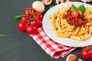 Etli makarna, domates sosu ve sebzeler masada.