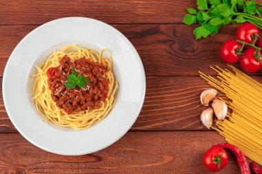 Etli makarna, domates sosu ve sebzeler masada.