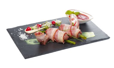 Koyu tabakta soslu ızgara domuz pastırması ile sarılmış kuşkonmaz. yaratıcı fotoğraf.