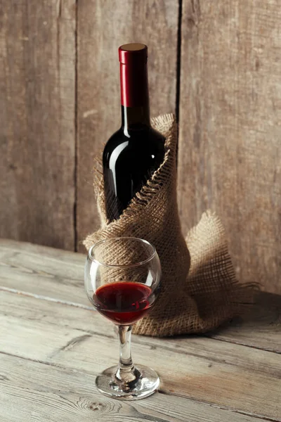 Glass and bottle with delicious red wine on table against wooden background — Stock Photo, Image