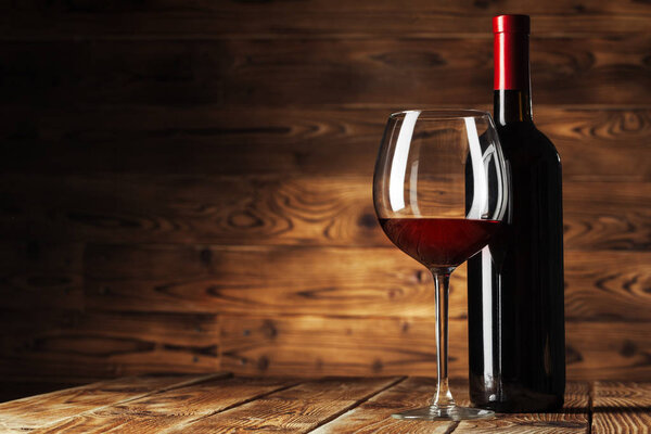 Glass and bottle with delicious red wine on table against wooden background. Creative photo.