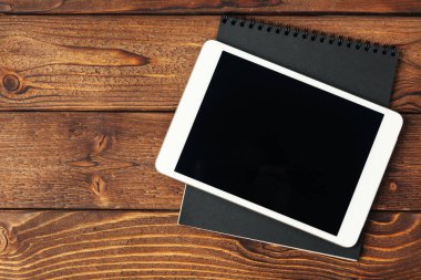 Tablet with notepad on wooden background. Creative photo.