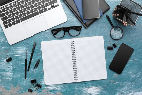 Opened notebook and other office equipment such as computer, pencil, and glasses on wooden office desk.