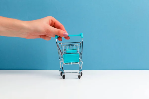 Winkelwagen trolley bij de hand op witte en blauwe achtergrond. Zijaanzicht. Winkelconcept. — Stockfoto