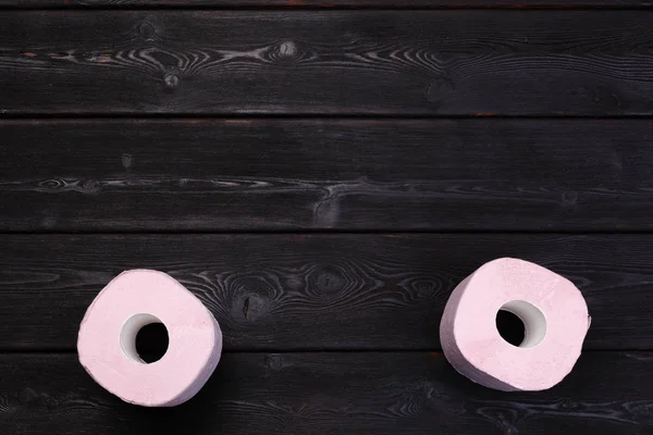 Pastel pink toilet paper rolls on black wooden background — Stock Photo, Image