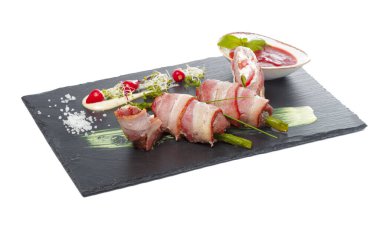 Koyu tabakta soslu ızgara domuz pastırması ile sarılmış kuşkonmaz.