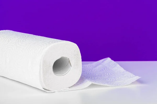 Roll of paper towel on table against purple background