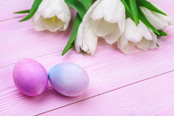 Pasen achtergrond met kleurrijke eieren en tulpen over roze hout. Bovenaanzicht met kopieerruimte. Creatieve foto. — Stockfoto