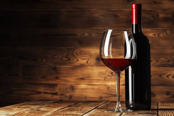 Glass and bottle with delicious red wine on table against wooden background