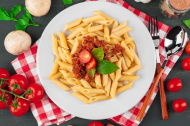 Etli makarna, domates sosu ve sebzeler masada.