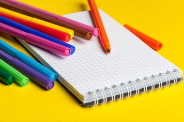 Parlak sarı arka plan üzerinde keçeli kalemler ve boş not defteri