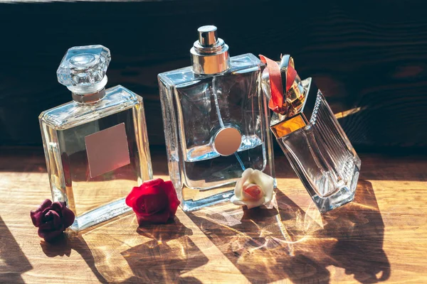 Several bottles with perfume in rays of sunshine on wooden table — Stock Photo, Image