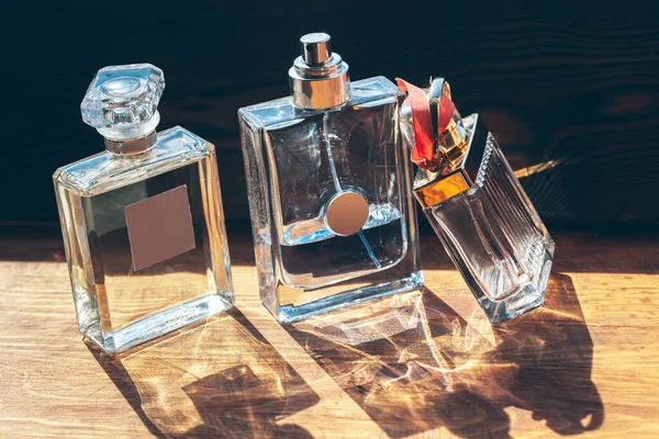 Mehrere Flaschen mit Parfüm in Sonnenstrahlen auf Holztisch — Stockfoto