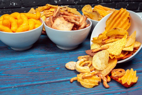 Tipos diferentes de comida chatarra, palos salados, galletas saladas en la mesa de madera en bodegón — Foto de Stock