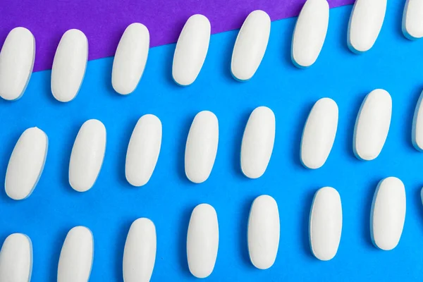 Píldoras blancas caóticamente dispersas sobre un patrón de fondo azul. Píldoras blancas fondo. Textura para el diseño — Foto de Stock