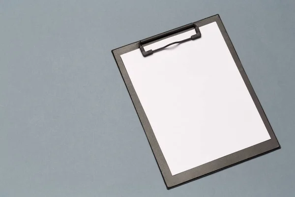 Black clipboard with empty sheets of paper on a dark table — 图库照片