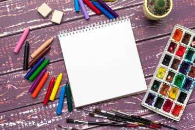 Çizim aletleri, sabit malzemeler, sanatçının çalışma yeri. Suluboya resimler ve ahşap masadaki boş not defteri.