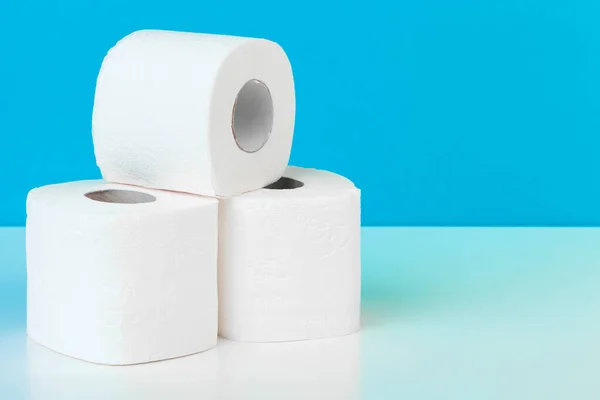 Tres rollos de papel higiénico aislados en mesa blanca con fondo azul — Foto de Stock