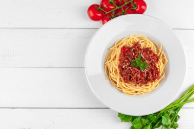 Etli makarna, domates sosu ve sebzeler masada.