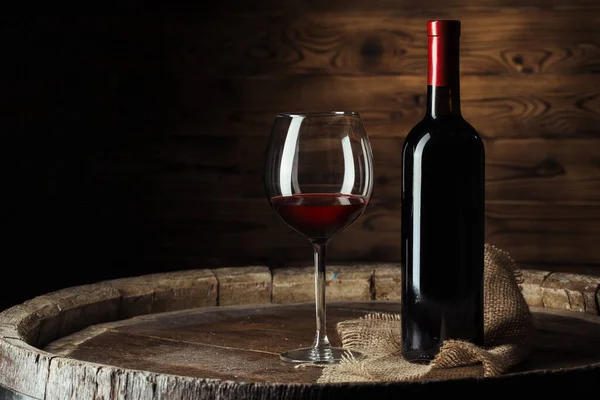 Bottle and glass of red wine on wooden barrel shot with dark wooden background — Stock Photo, Image