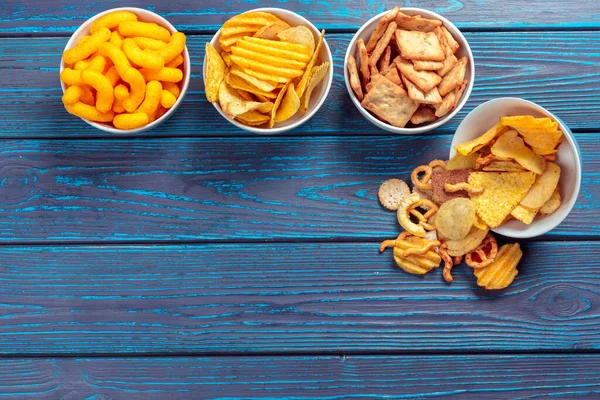 Tipos diferentes de comida chatarra, palos salados, galletas saladas en la mesa de madera en bodegón — Foto de Stock