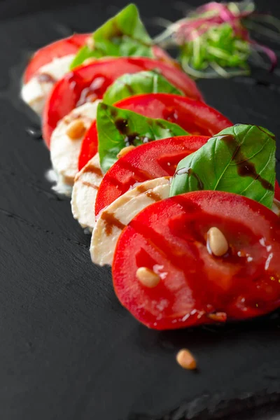 Свежий итальянский салат капрезе с моцареллой и помидорами на темной тарелке — стоковое фото