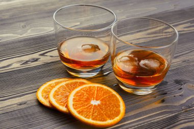 Koyu ahşap arka planda portakal meyveli viski bardağı.