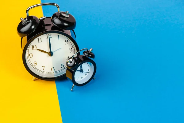 Relógio de alarme preto no bloco de cores fundo amarelo e azul — Fotografia de Stock