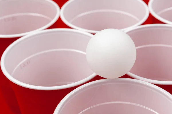 Copas y bola de plástico sobre fondo rojo. Cerveza pong juego — Foto de Stock
