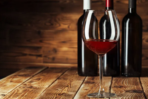 Glass and bottle with delicious red wine on table against wooden background — Stock Photo, Image