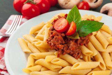 Etli makarna, domates sosu ve sebzeler masada.