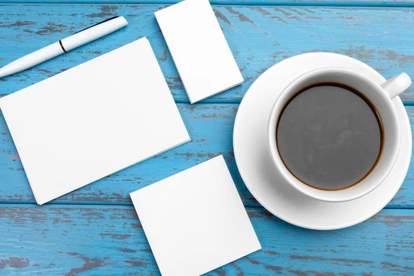 Schreibwarenattrappe auf blauem Schreibtisch. Draufsicht auf Papier, Visitenkarte, Block, Stifte und Kaffee. — Stockfoto