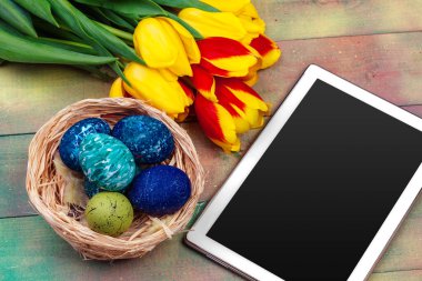 mesaj için tablet ekranı ve renkli laleler ve ahşap zemin üzerinde paskalya yumurtaları
