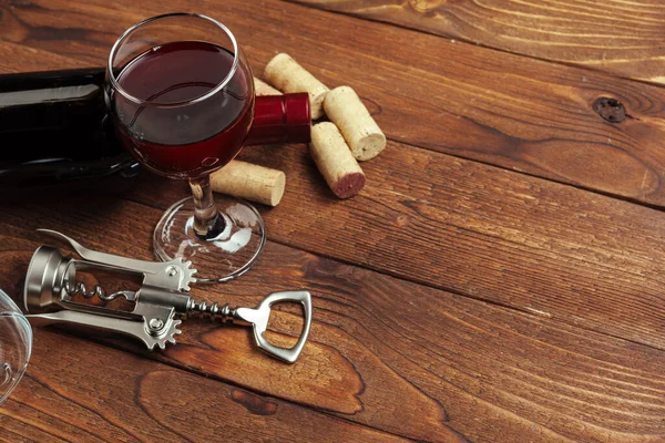 Red wine bottle, wine glass and corkscrew on wooden table background — Stock Photo, Image