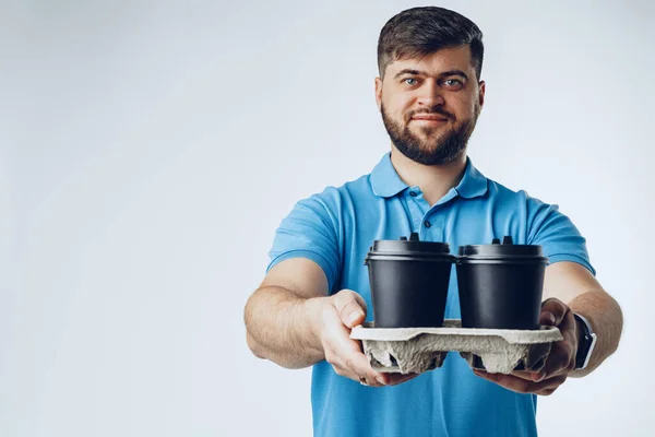 Hombre trabajador de la cafetería dando tazas de café para llevar sobre fondo gris — Foto de Stock